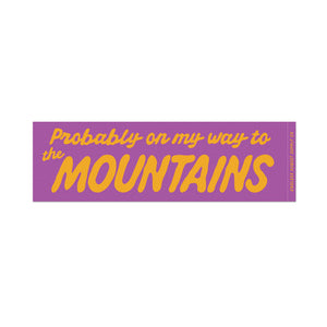 A rectangular bumper sticker with a purple background and yellow text that reads 'Probably on my way to the MOUNTAINS'.